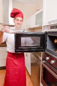 Man in chef hat standing in front of microwave door